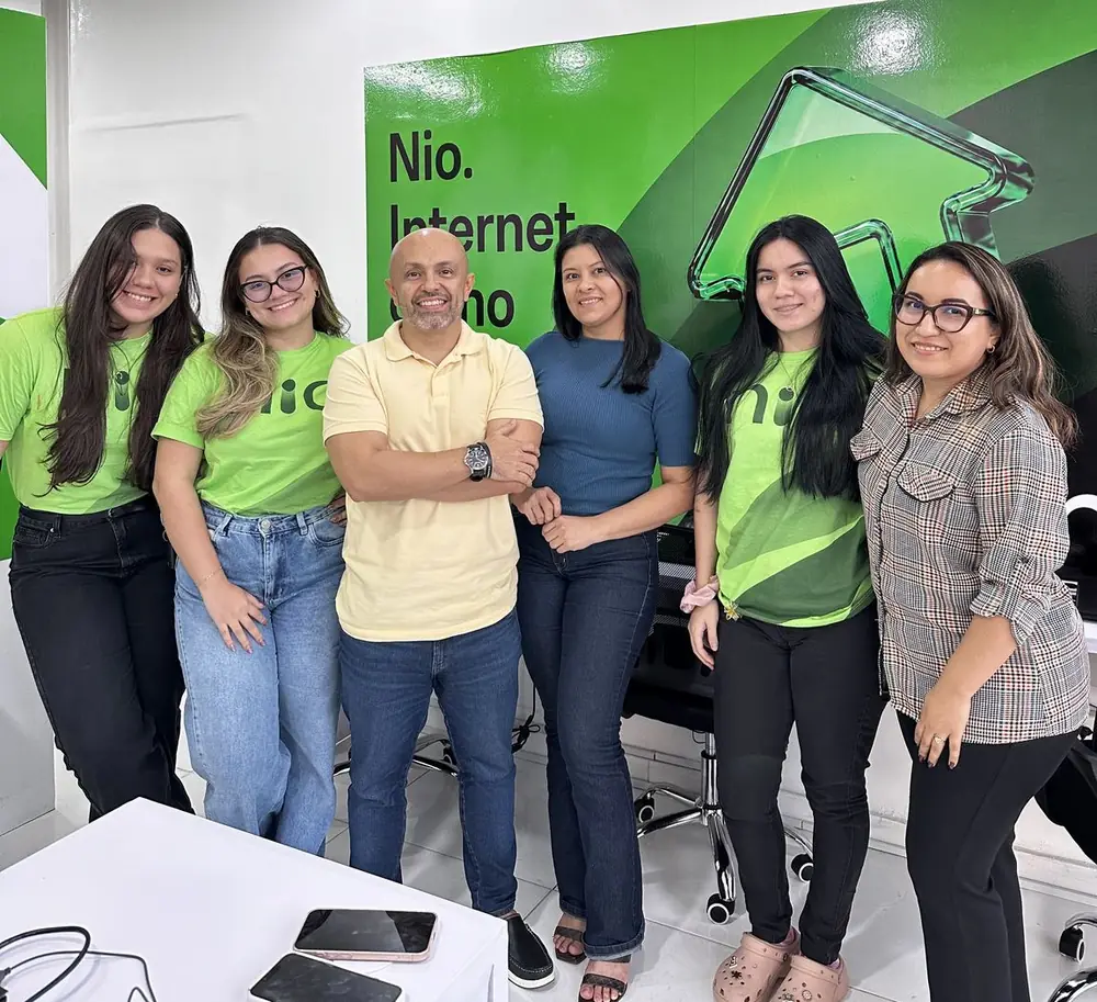 Equipe da Conecta GDTECH no escritório, em frente ao painel da NIO